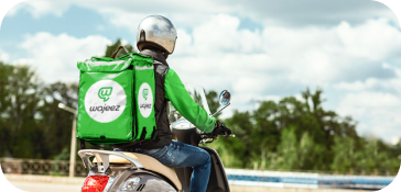 A delivery man riding his scooter with a green Wajeez box on his back.